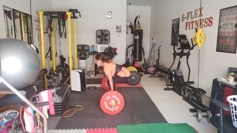 A client mid-deadlift on the S-Flex Fitness training floor, surrounded by plates, bands, and a heavy bag
