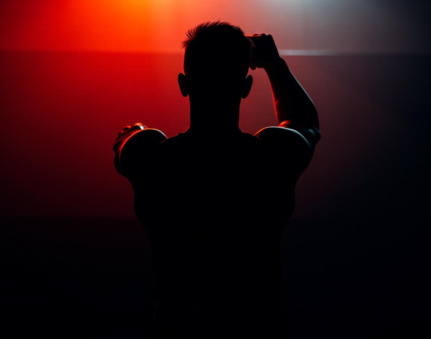 Silhouette of an athlete swinging a kettlebell under a warm red rim light